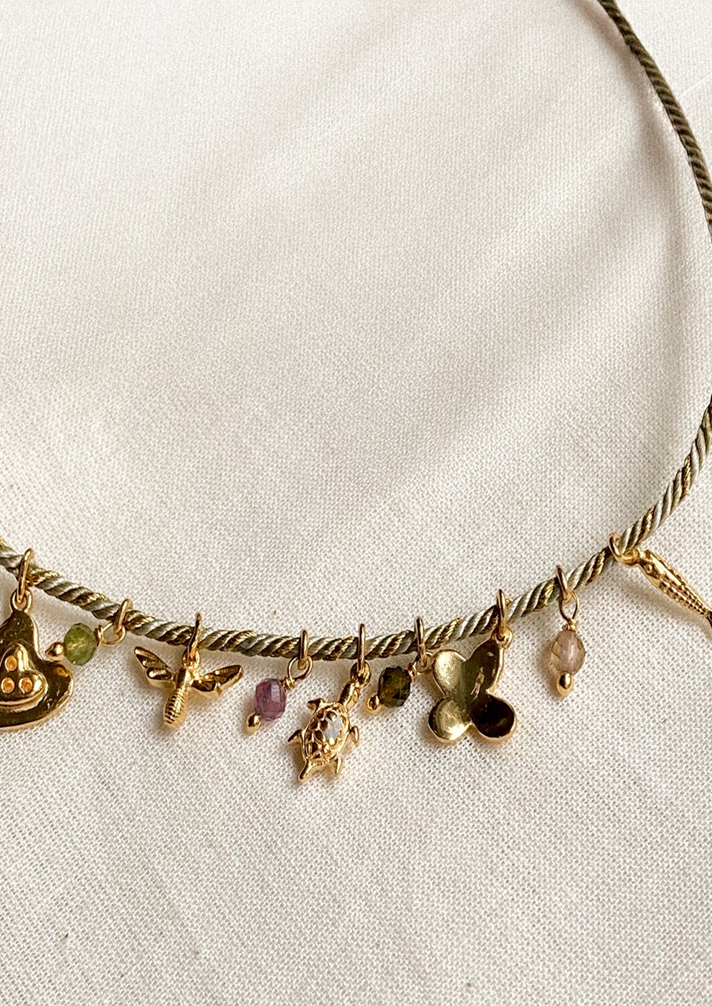 Gold necklace with various charms on a white fabric background