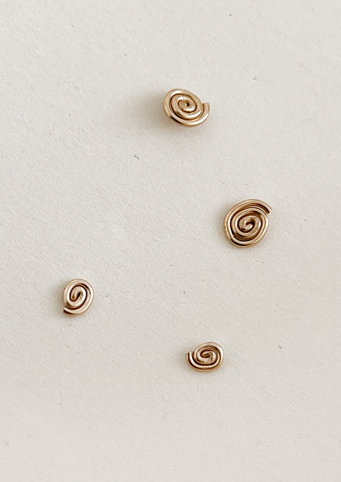 Four gold spiral earrings on a light gray background