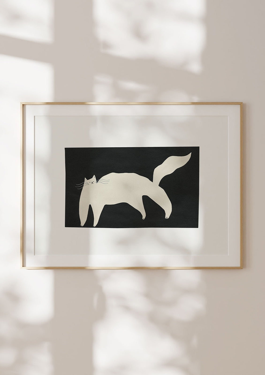 Framed artwork of a white cat silhouette on a black background, casting a shadow on a light-colored wall.