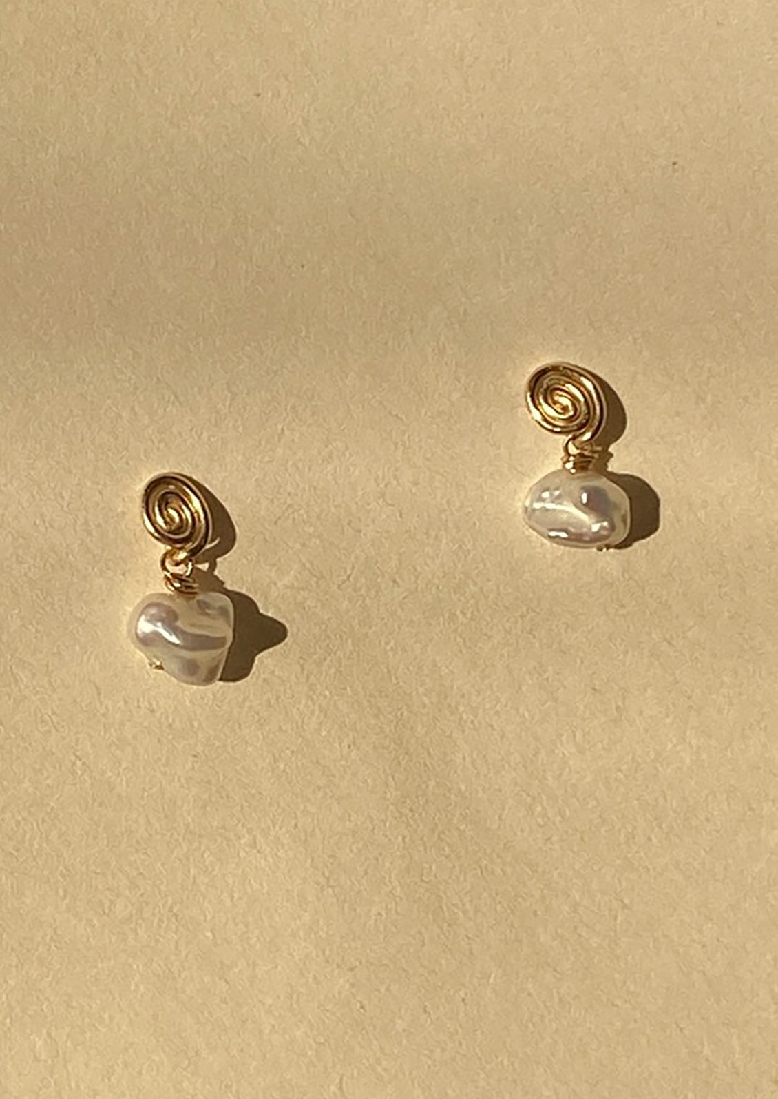 Pair of pearl earrings with gold spiral accents on a beige background