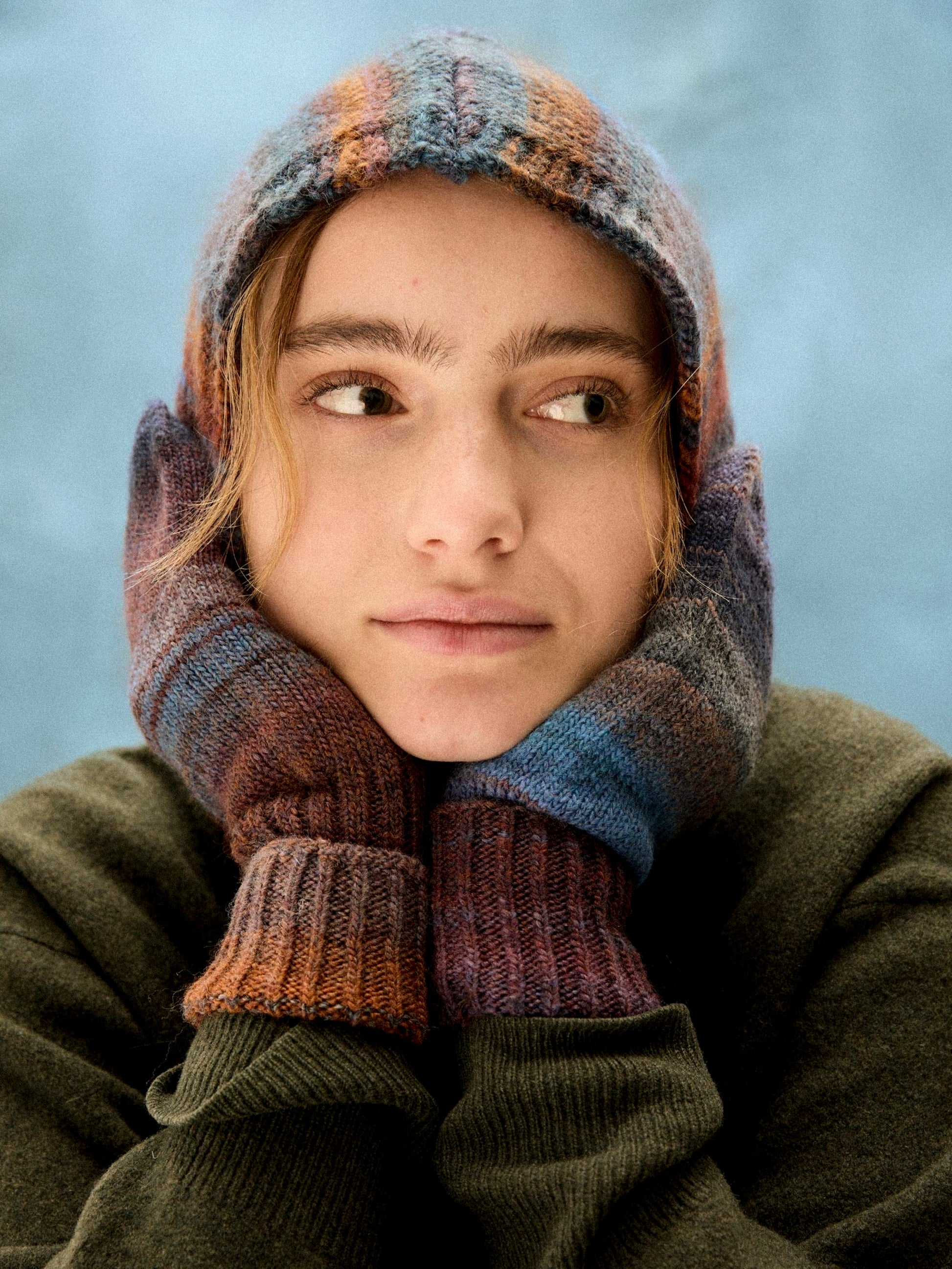 Person wearing a colorful knitted hat and gloves against a blue background