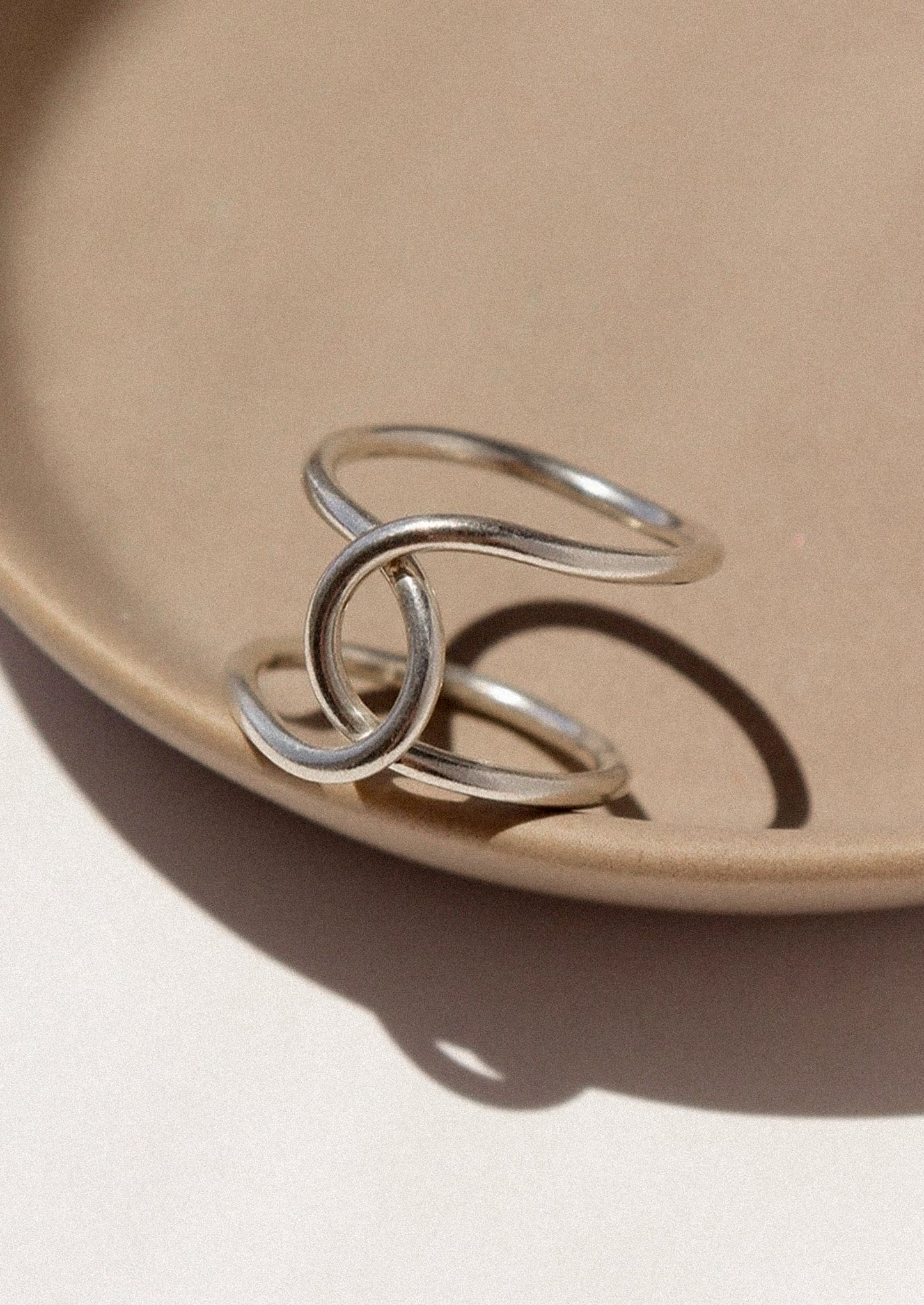 Silver ring with interlocking loops on a beige plate
