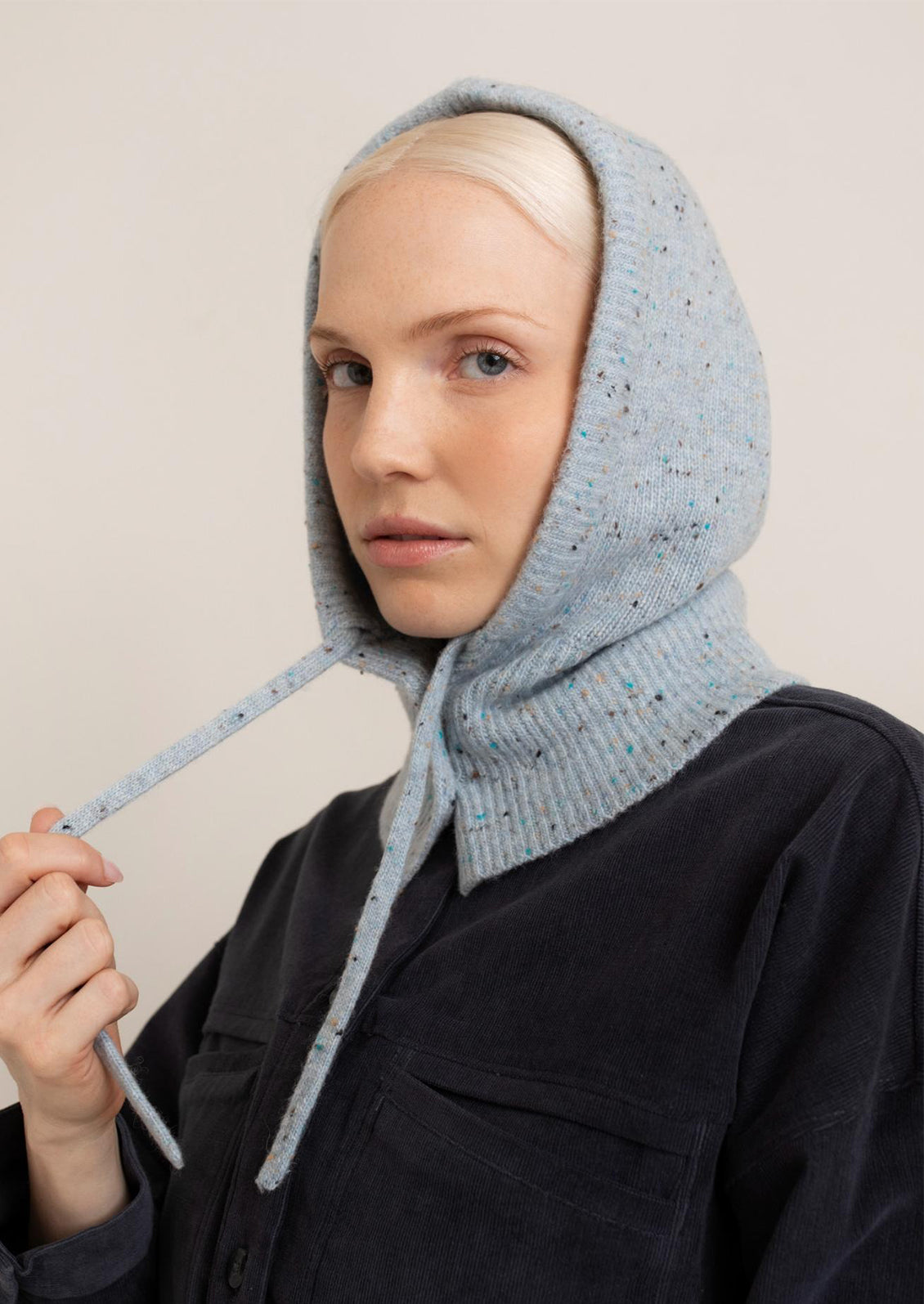 Person wearing a light blue knitted hood against a plain background