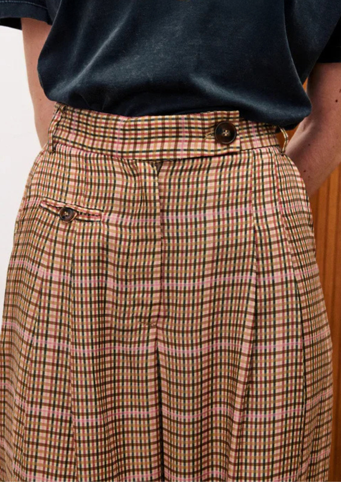 Plaid trousers with button details worn by a person against a neutral background