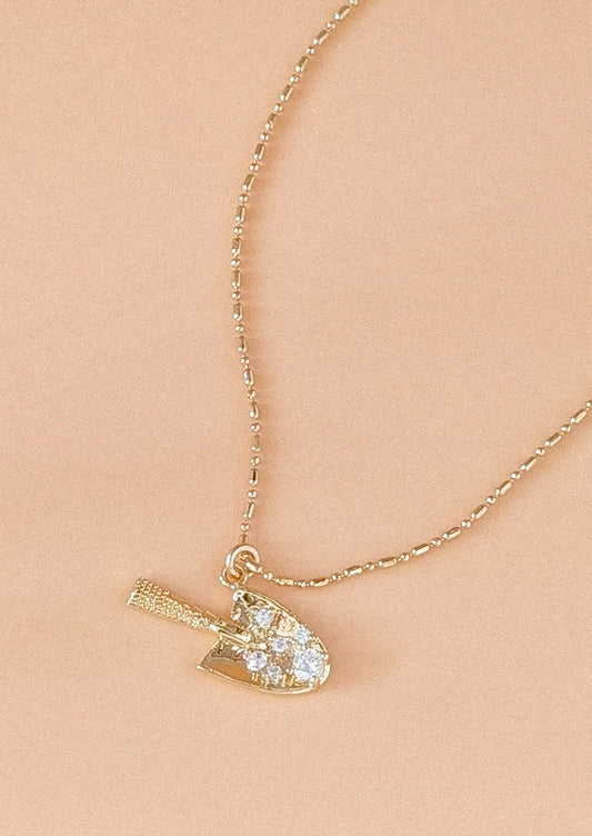 A gold necklace with garden trowel pendant charm.