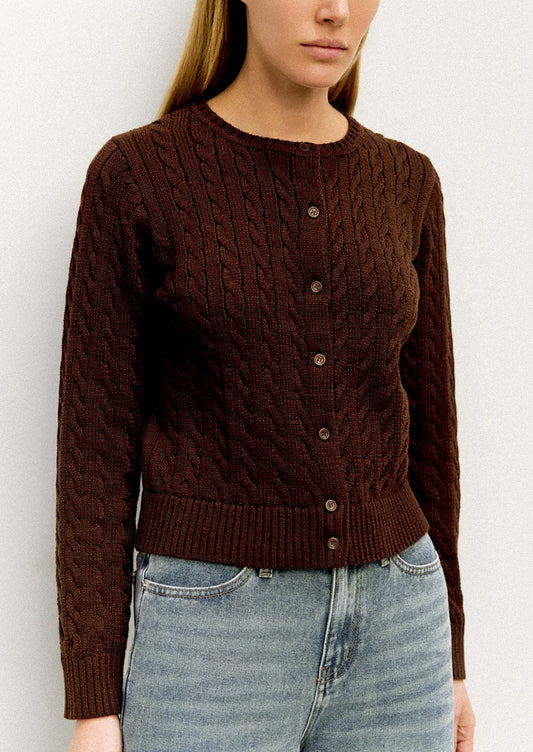 Person wearing a brown cable knit sweater with buttons and light blue jeans against a white background