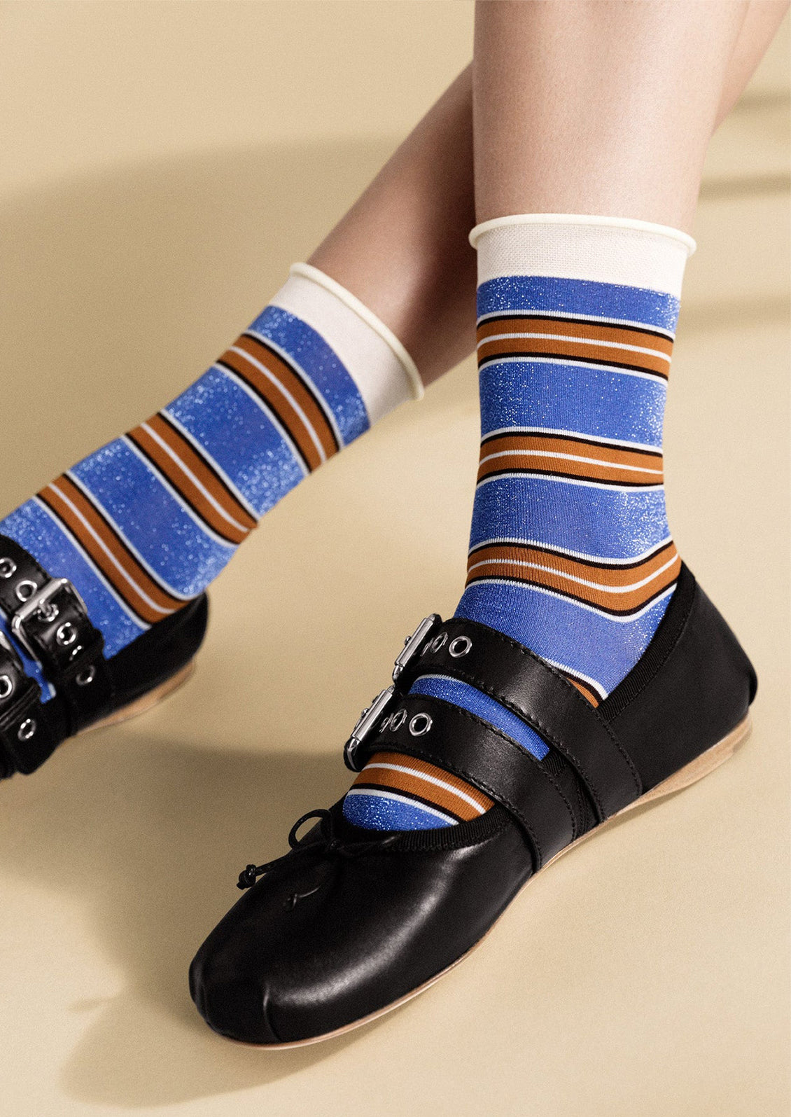 Striped socks with blue, brown, and white pattern worn with black shoes on a beige background