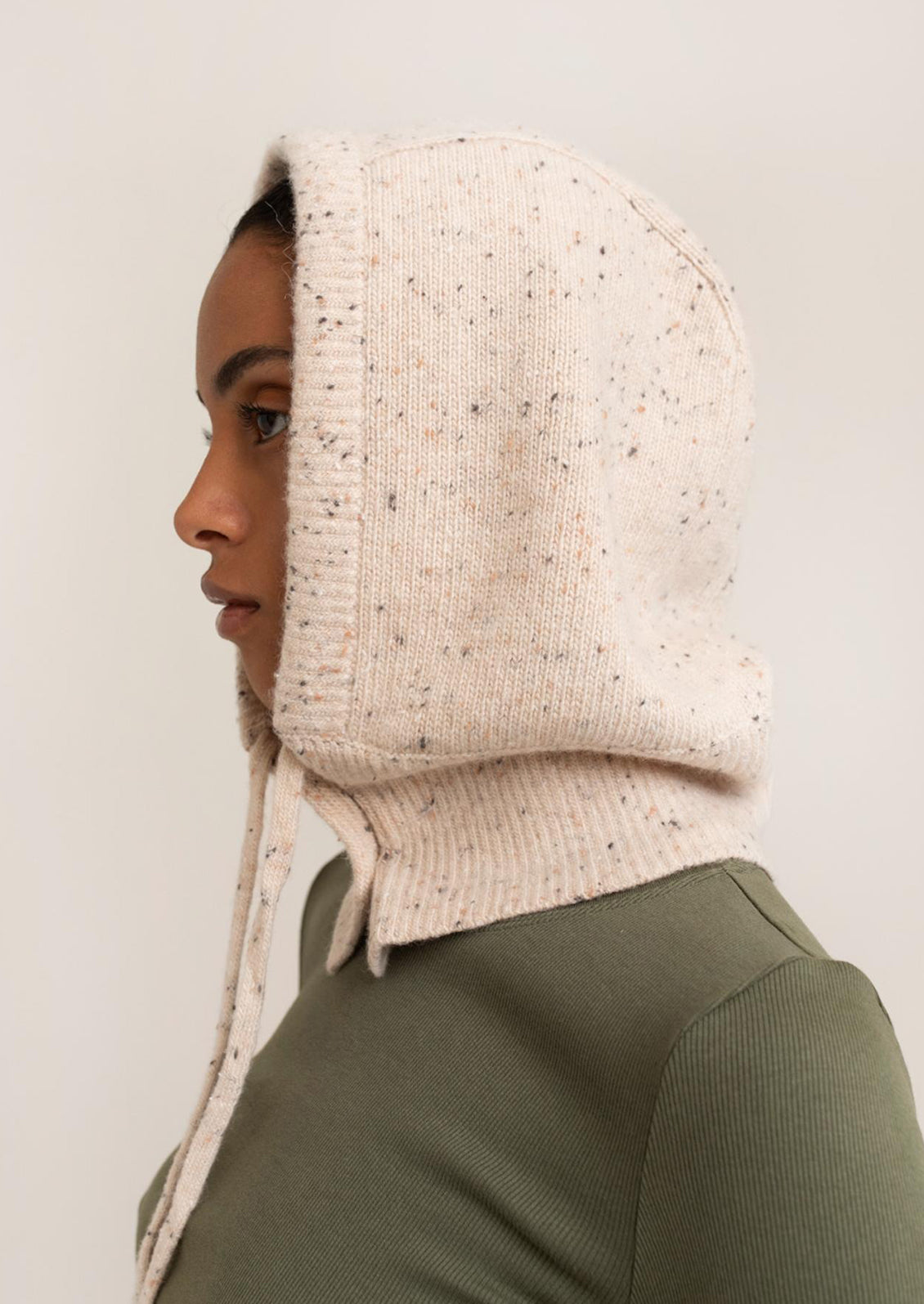 Person wearing a beige knitted hood against a plain background