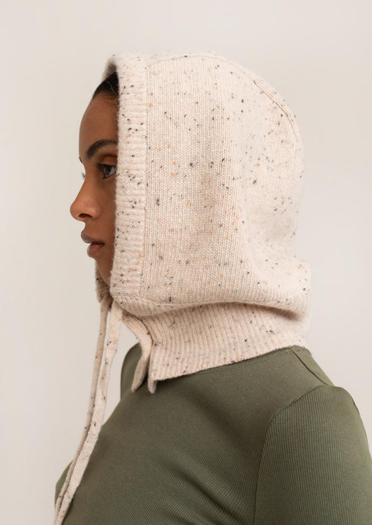 Person wearing a beige knitted hood against a plain background