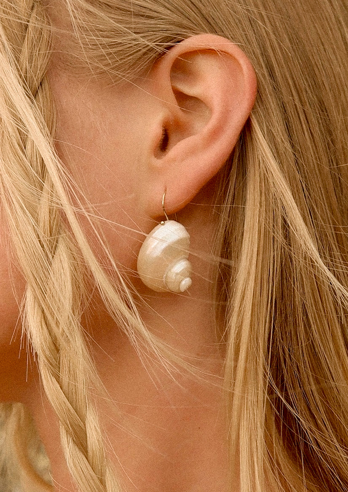 Close-up of a person wearing a shell earring with blonde hair.