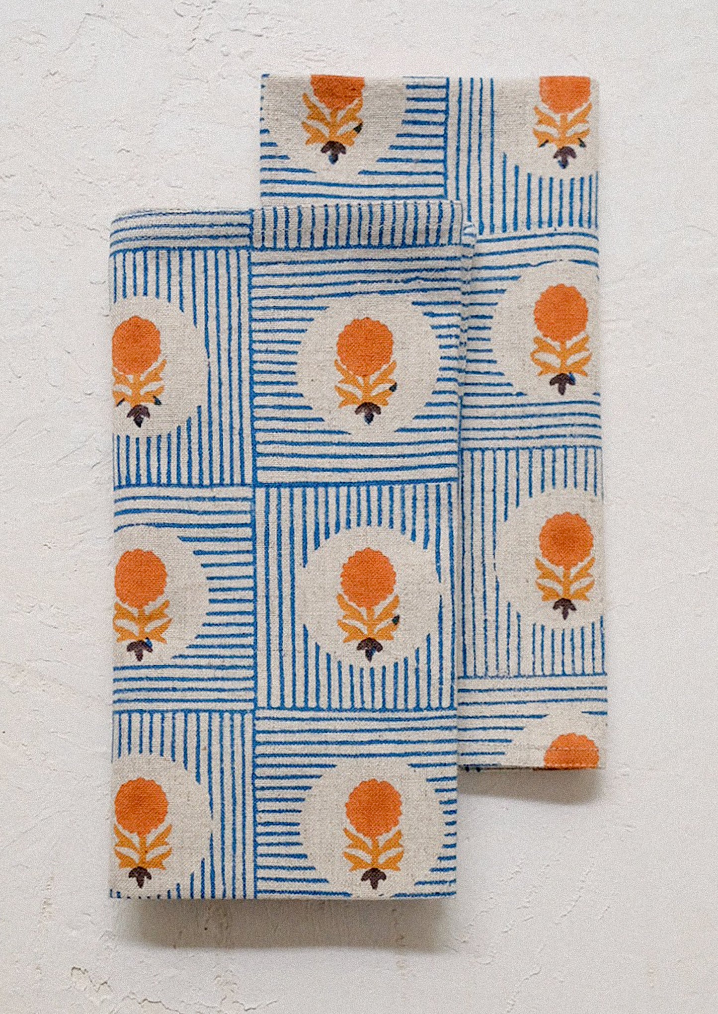 A folded cloth napkin with blue stripe and orange floral pattern.