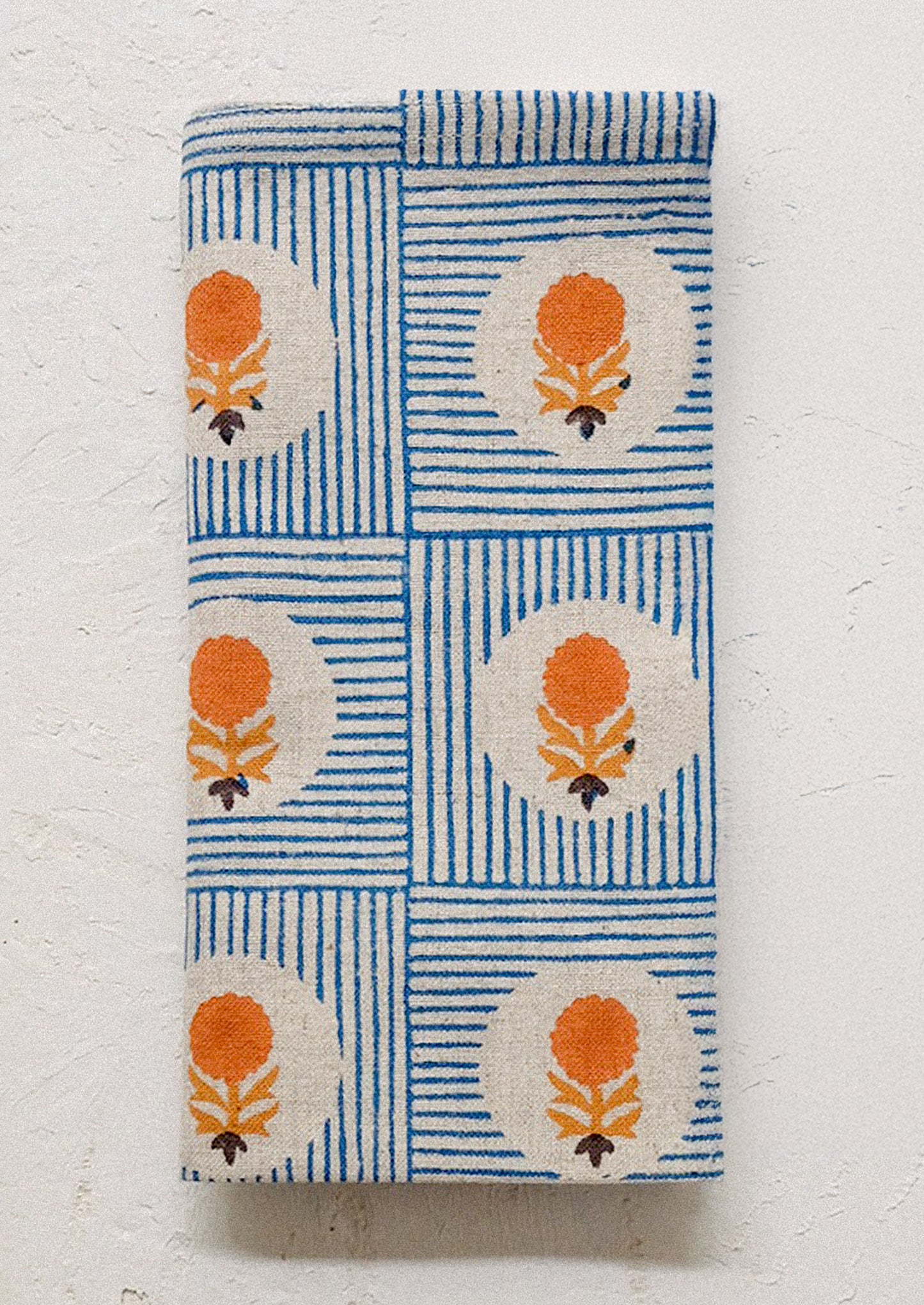 A folded cloth napkin with blue stripe and orange floral pattern.