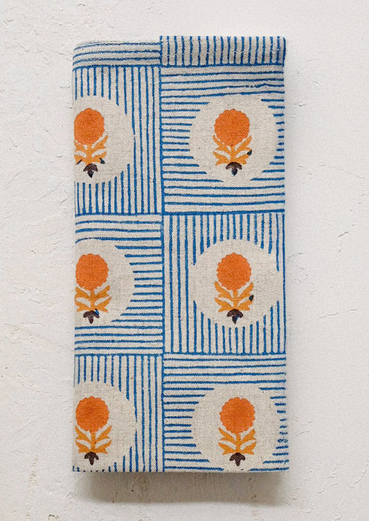 A folded cloth napkin with blue stripe and orange floral pattern.