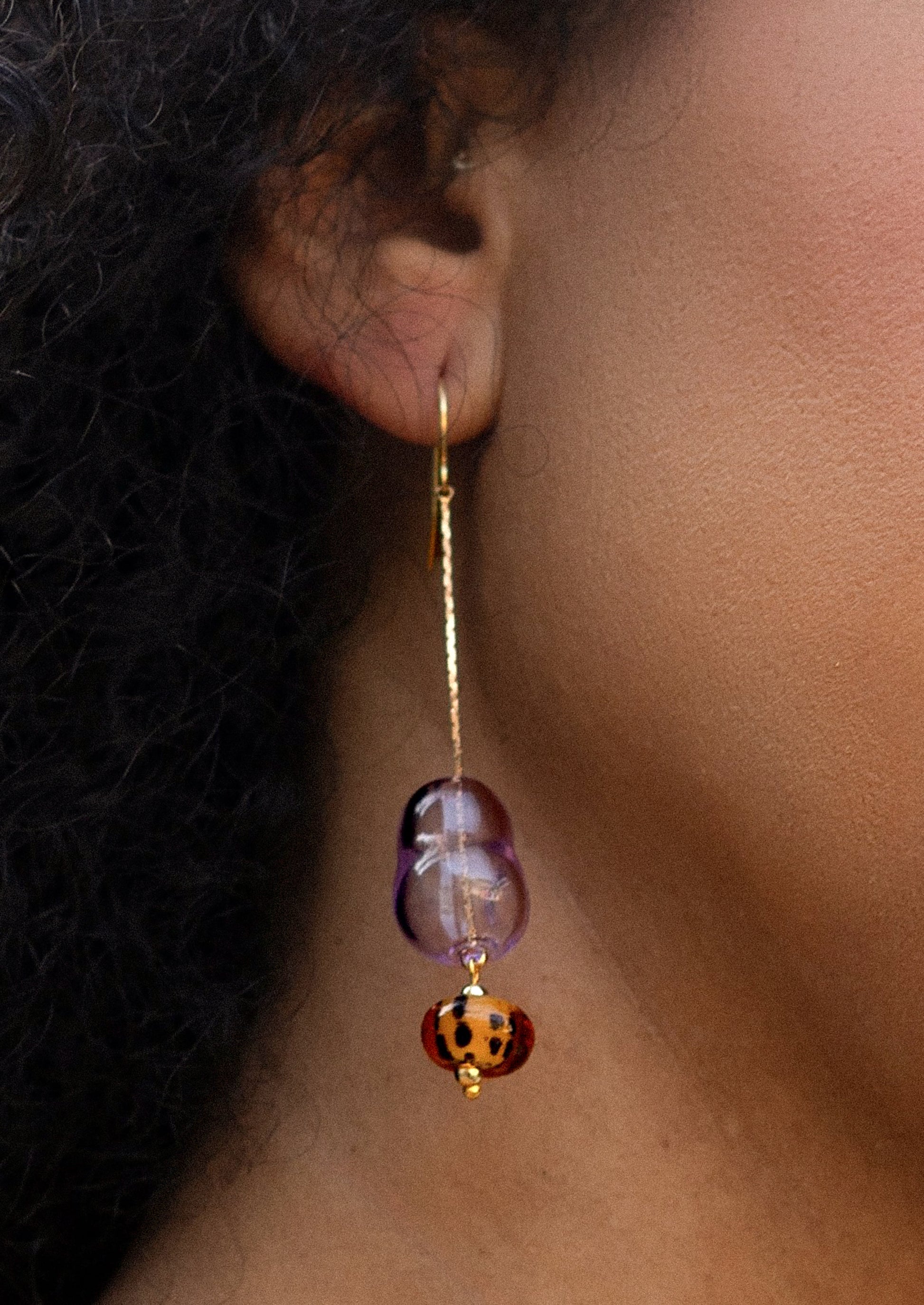 Earring with purple and orange beads worn by a person with dark hair.