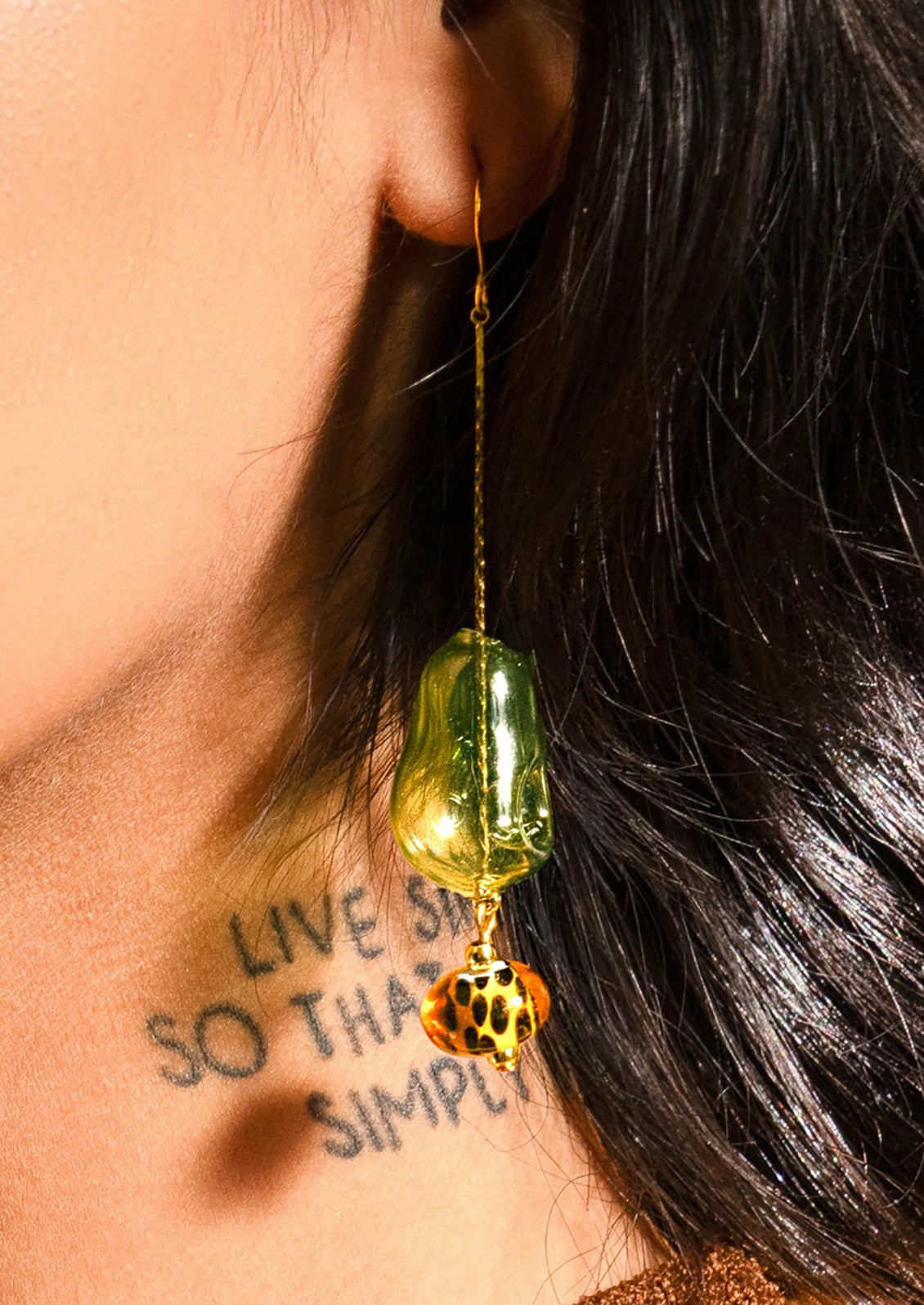 Close-up of a person wearing a green and gold earring with leopard print accents.