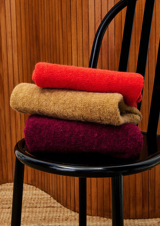 Stack of colorful folded scarves on a black chair against a wooden wall.