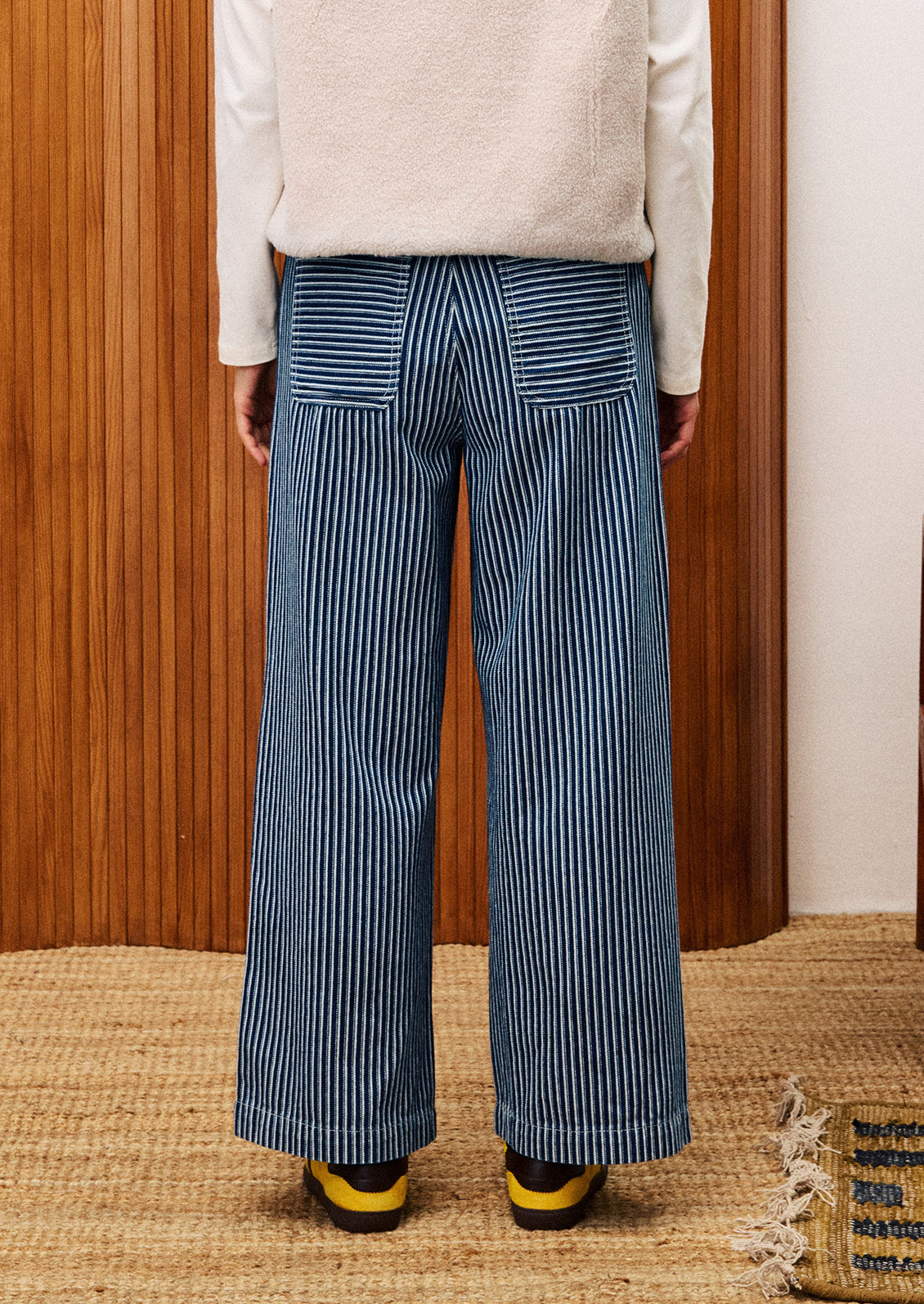 Person wearing blue striped pants standing against a wooden wall.