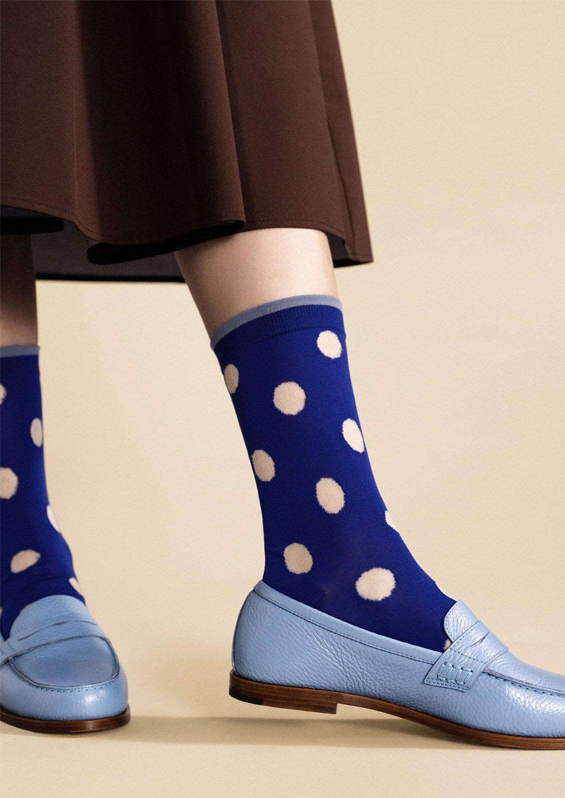 Blue socks with white polka dots worn with light blue shoes on a beige background