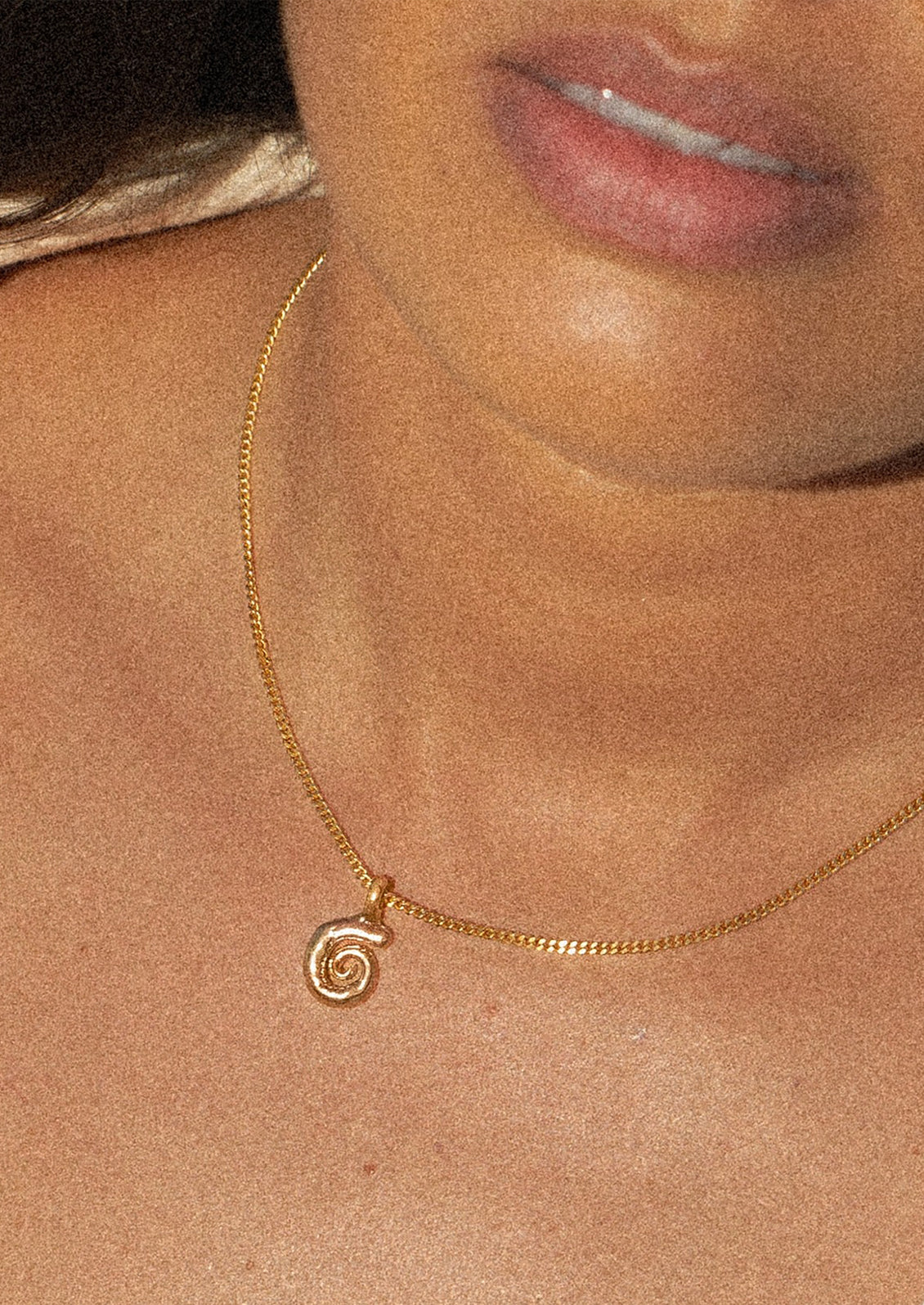 Gold necklace with a spiral pendant on a person's neck