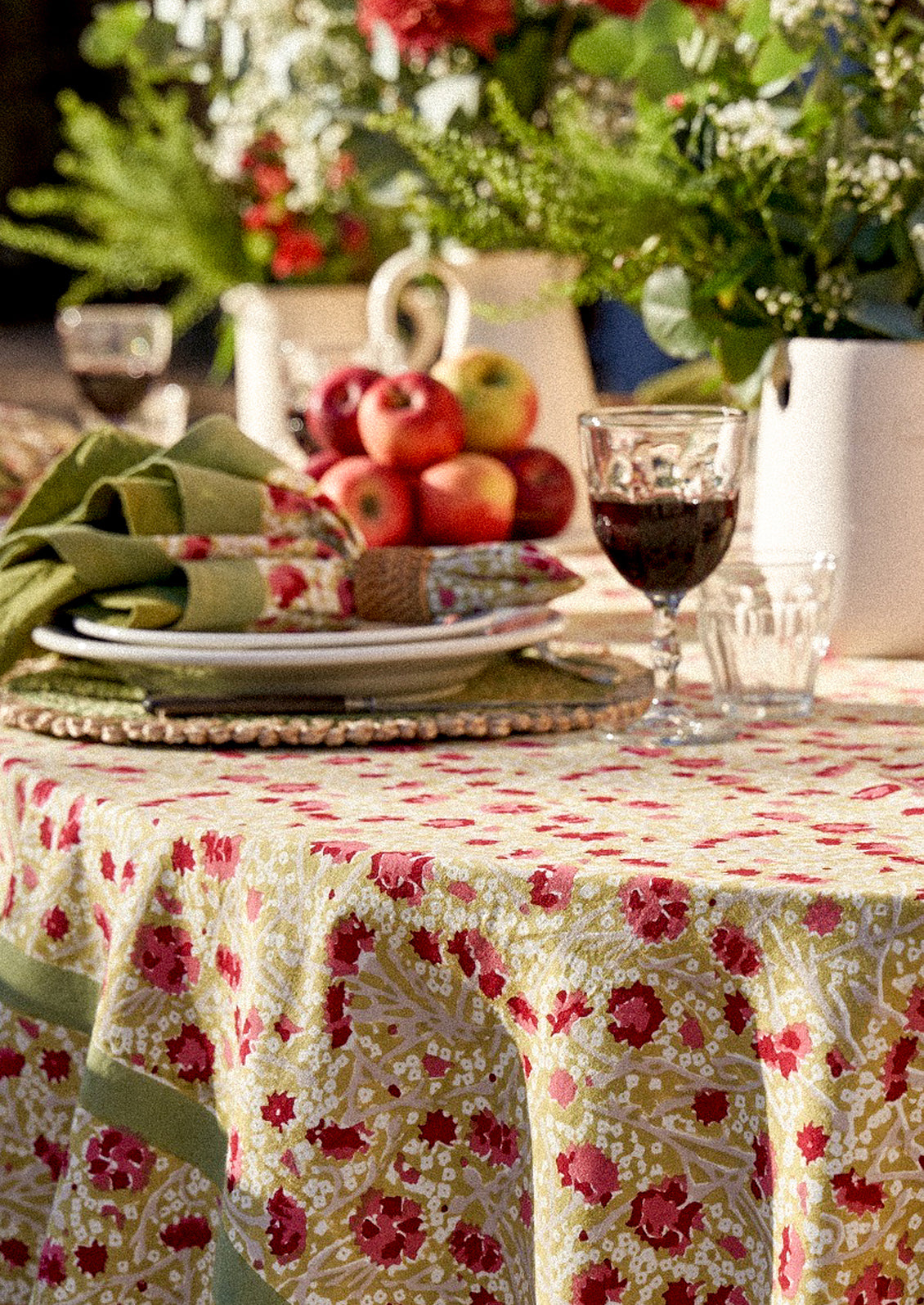 Decorative table setting with a floral tablecloth, apples, and wine glasses.