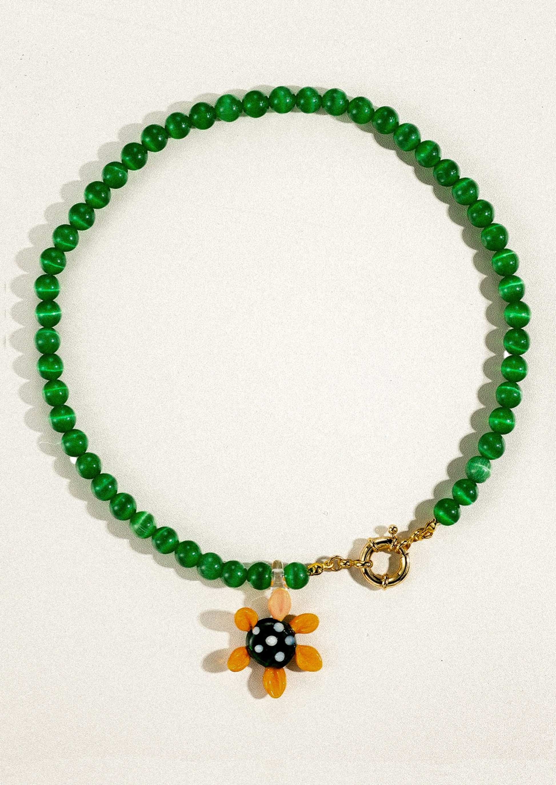 Green beaded bracelet with a sunflower charm on a white background
