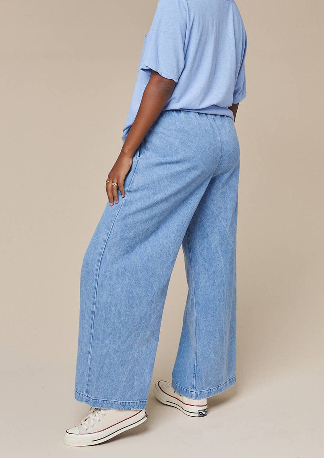 Person wearing light blue jeans and a matching top on a beige background