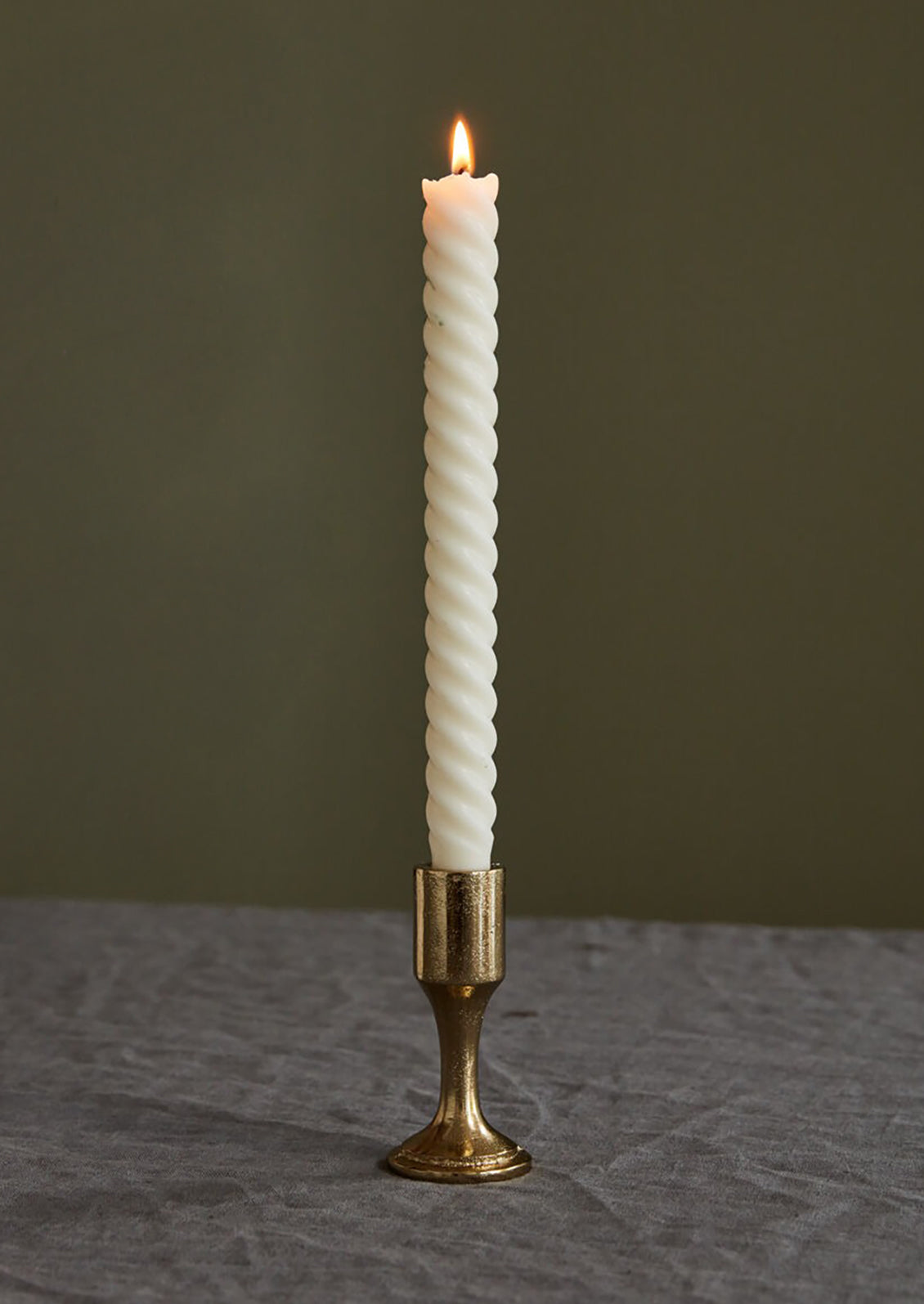 Twisted white candle in a brass holder on a dark surface with a dark background