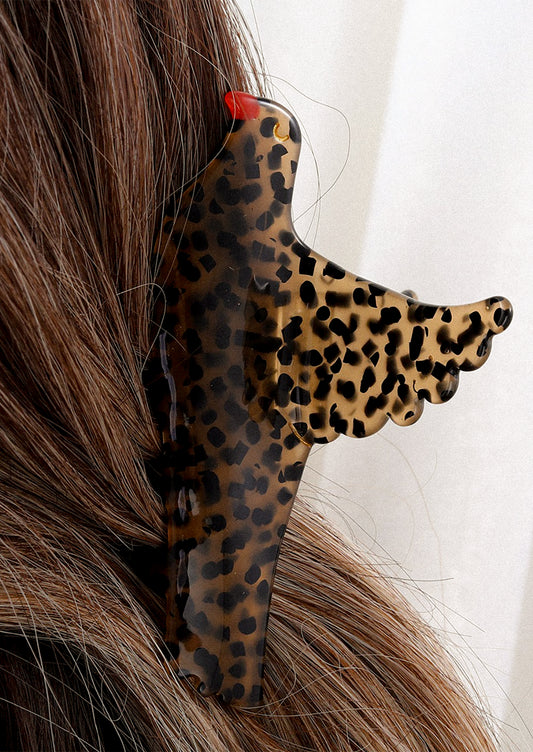 A person wearing a hair claw of brown bird with black spots and red beak.