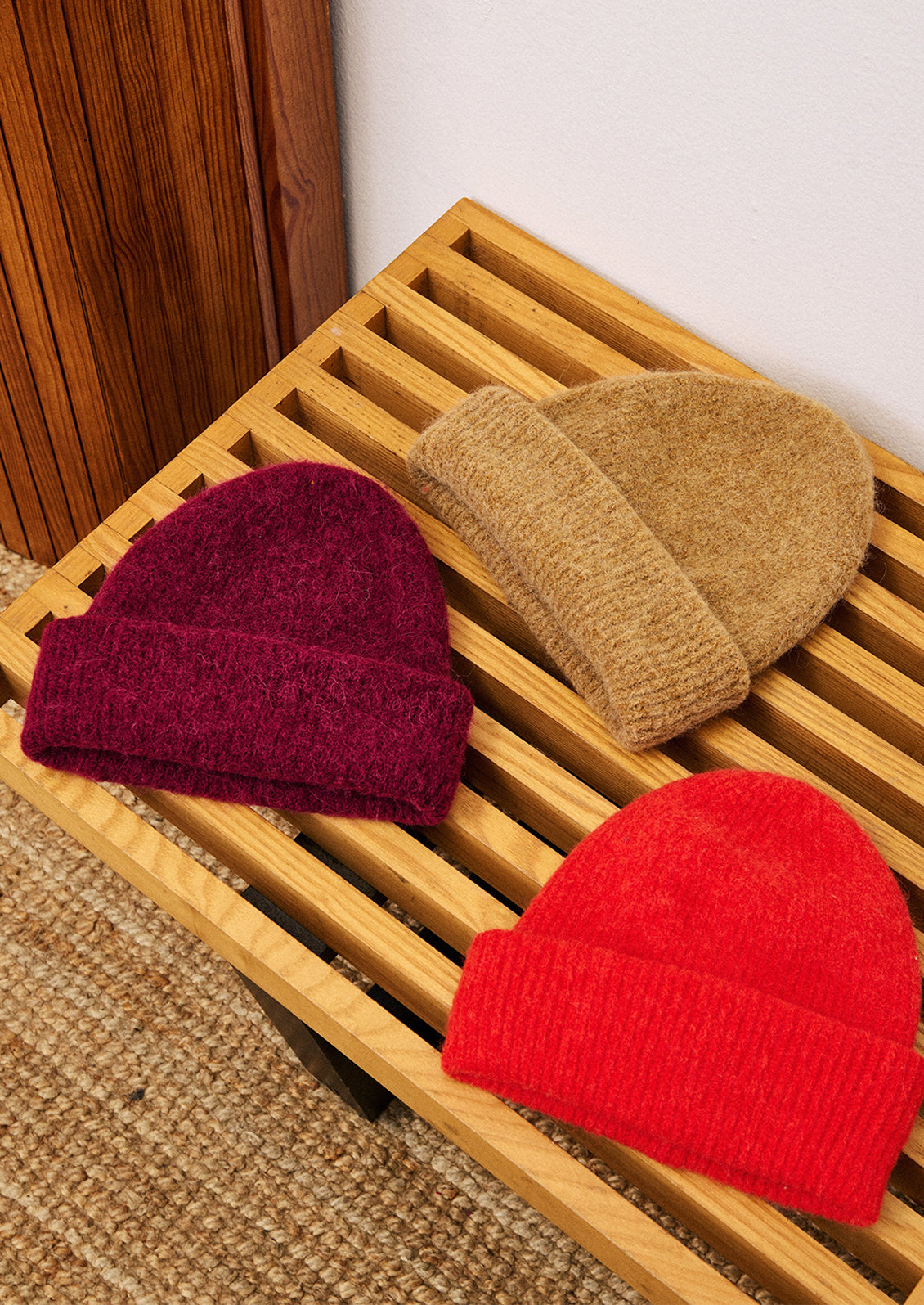 Three knit hats in red, brown, and burgundy on a wooden surface.