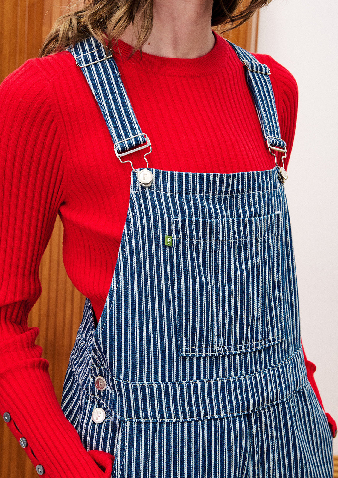 Person wearing a red sweater and blue striped overalls.