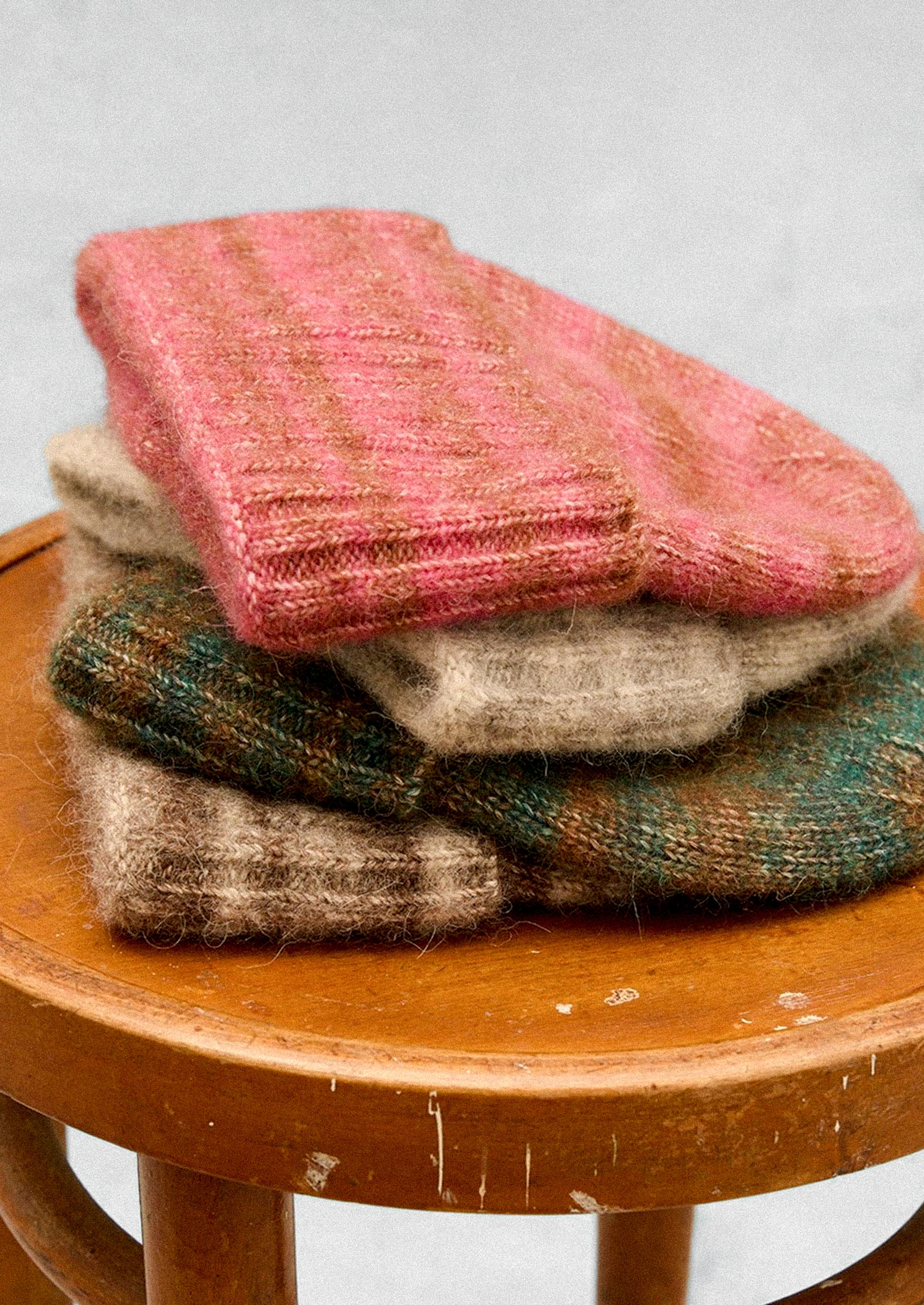Stack of colorful knitted items on a wooden stool against a light gray background