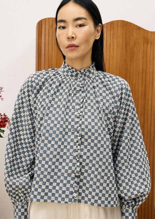 A woman wearing a ruffle neck blouse with embroidered white check pattern.