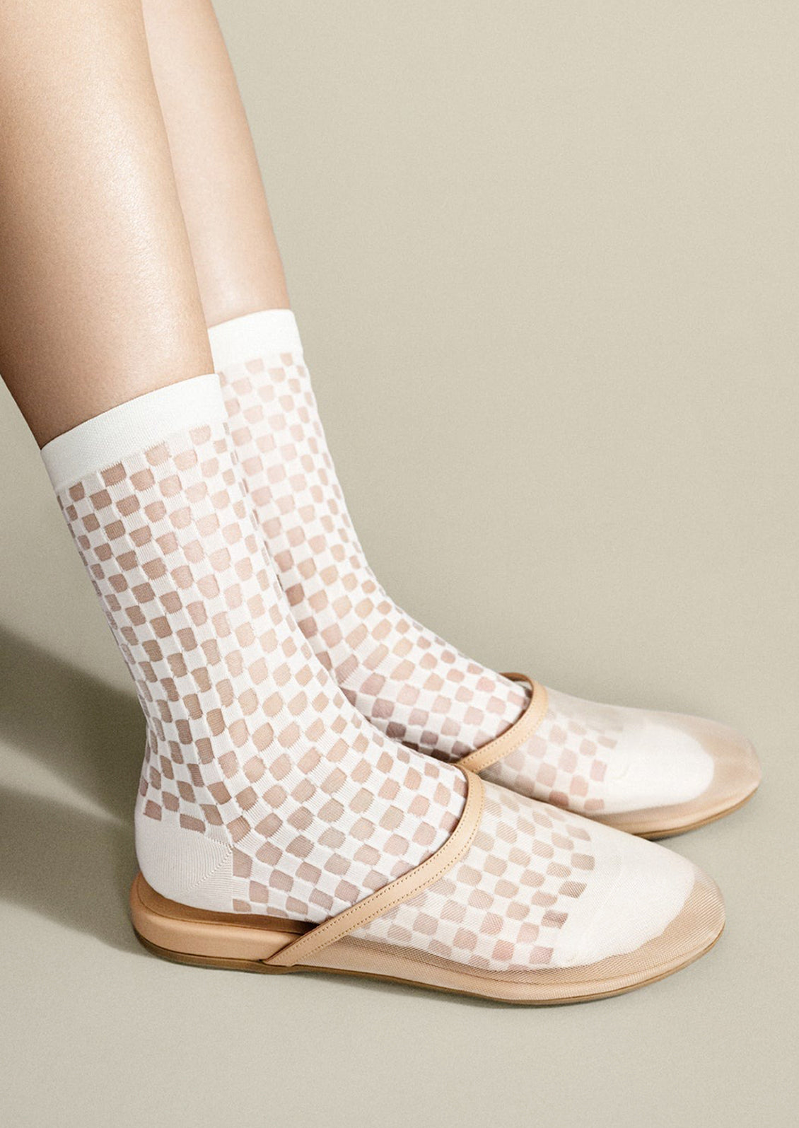 White fishnet socks with beige pattern worn with flat sandals on a neutral background