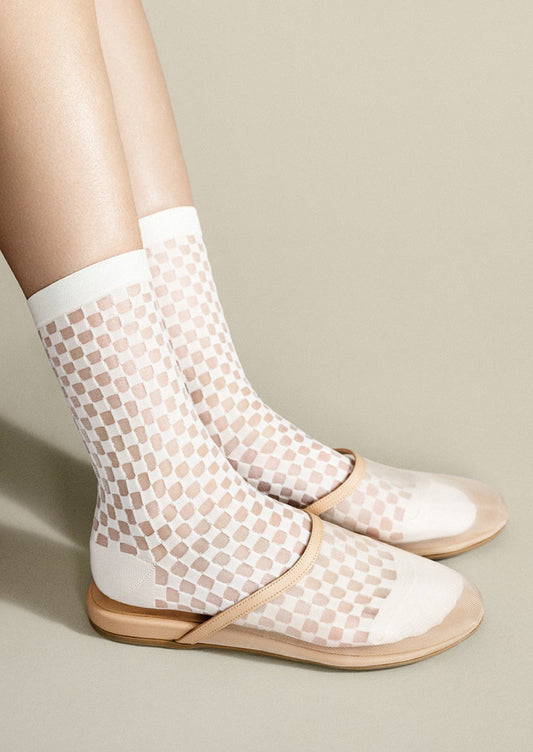 White fishnet socks with beige pattern worn with flat sandals on a neutral background
