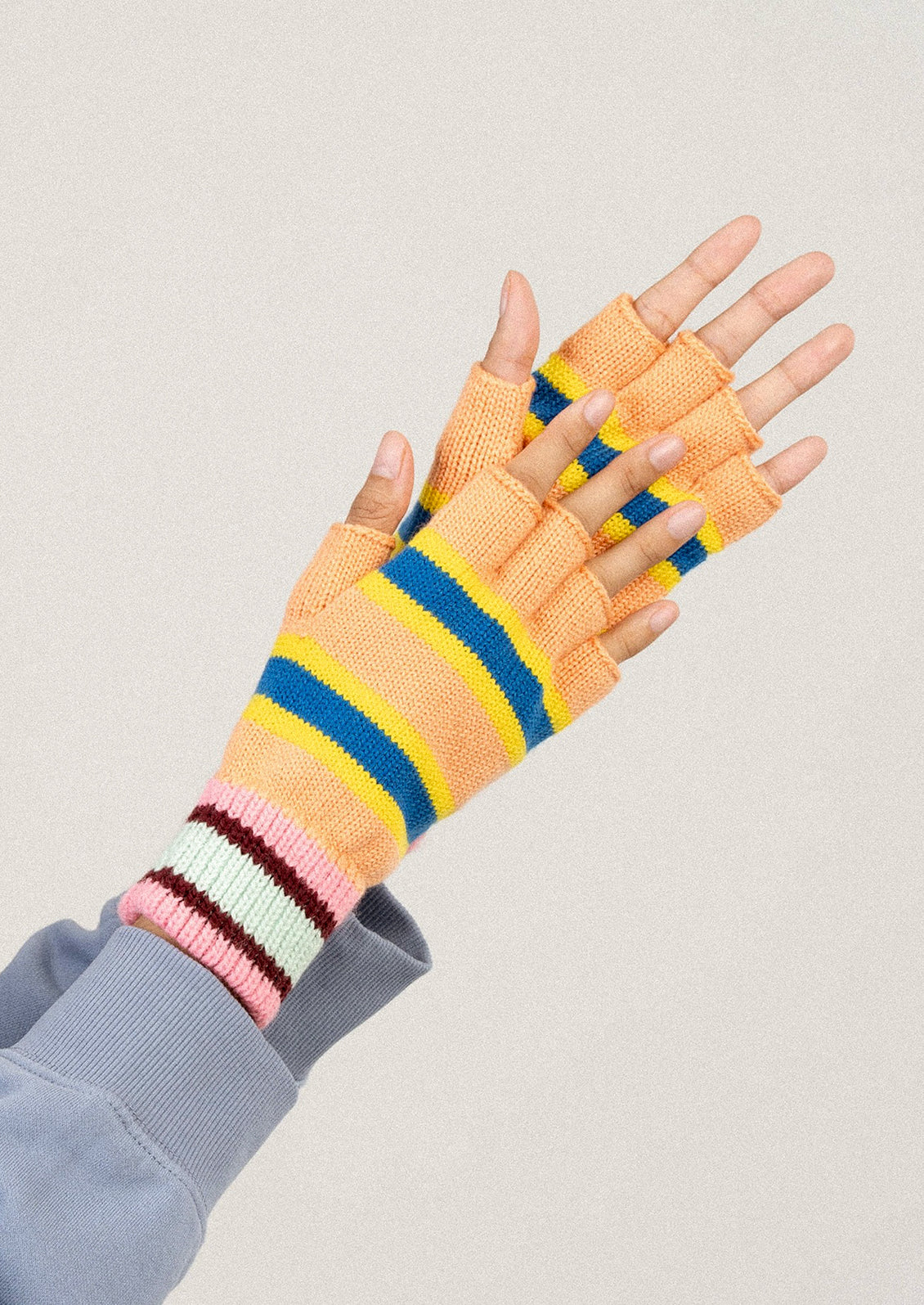 Colorful striped gloves worn on a neutral background