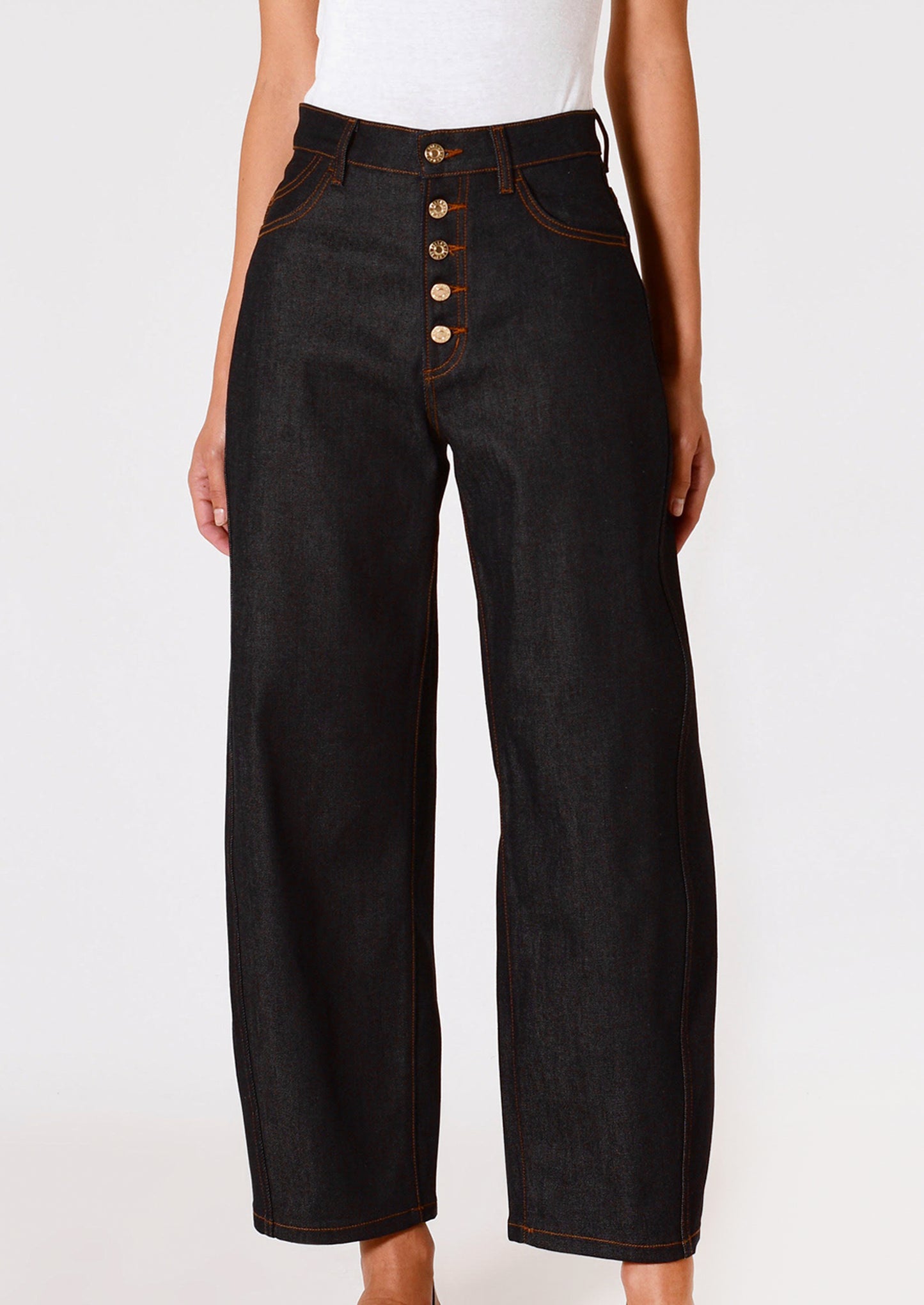 A person wearing a pair of dark rinse jeans with gold-tone exposed button fly and contrast orange stitching.