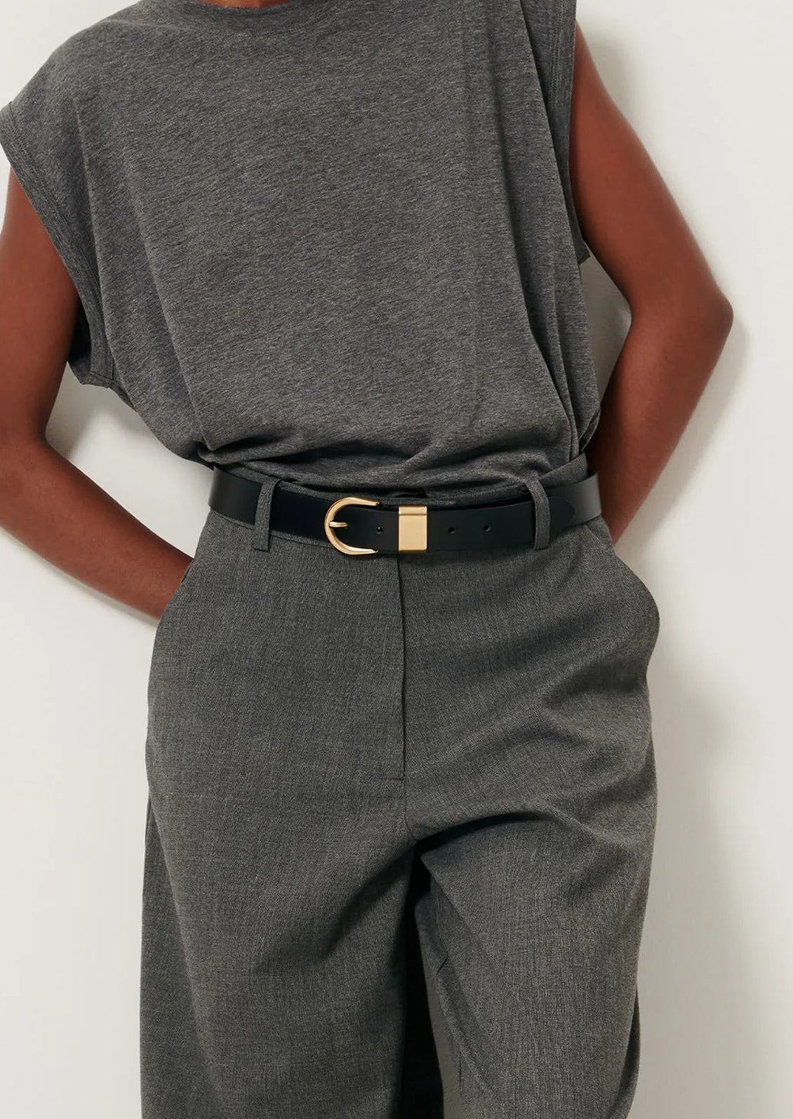 Person wearing a gray sleeveless top and high-waisted gray pants with a black belt on a white background