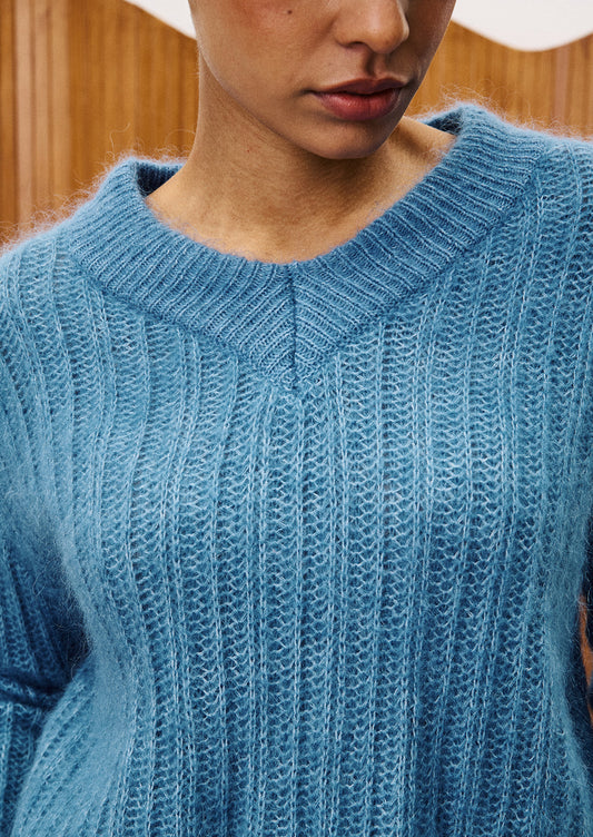 A woman wearing a dusty blue v-neck sweater.