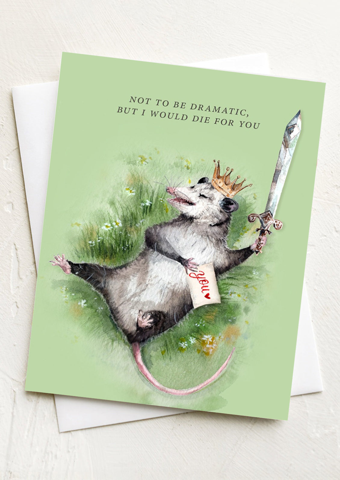 Greeting card with an illustration of a possum holding a sword and wearing a crown, on a light background.