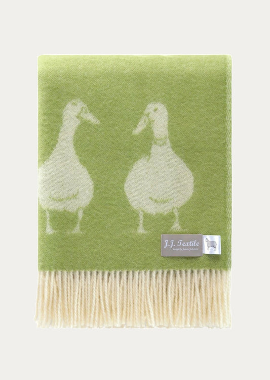 A green throw blanket with white duck motifs and cream-colored fringe.