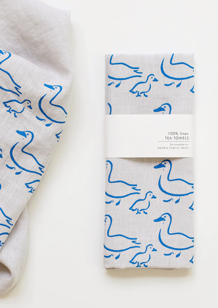 A grey linen tea towel with blue duck illustration print.