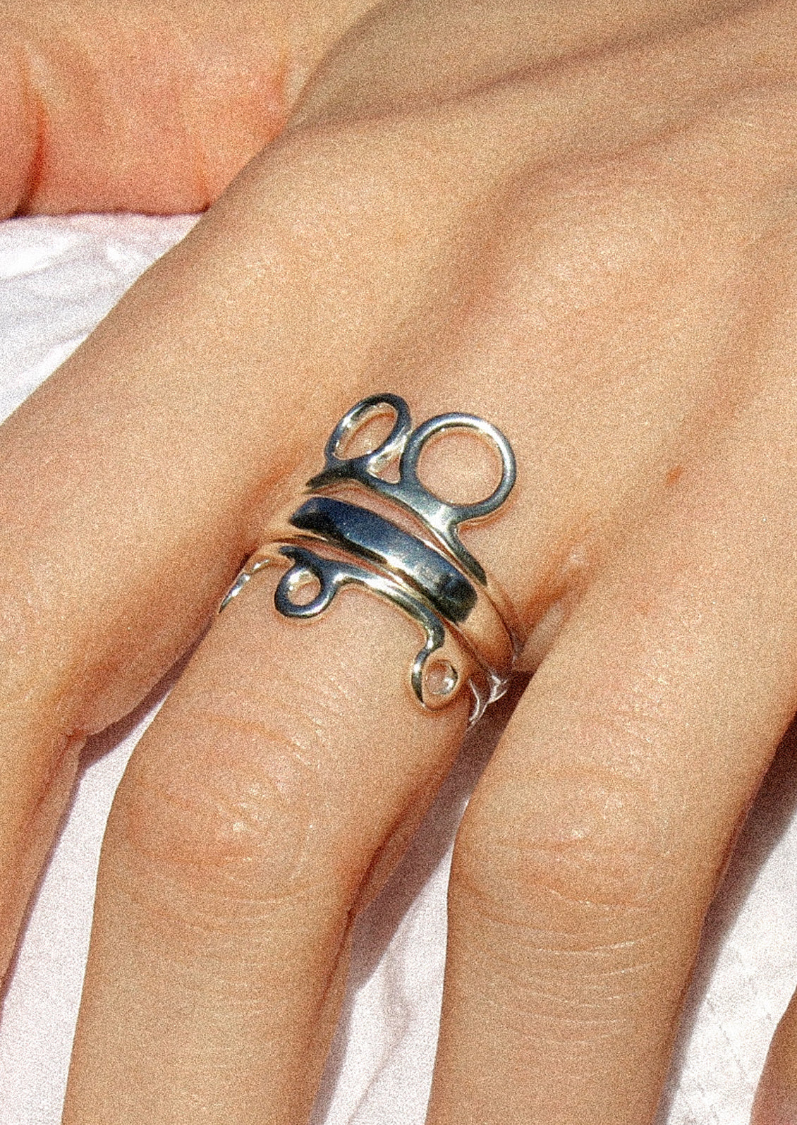 A sterling silver ring with a double circle design, on a person's hand with two other silver rings.