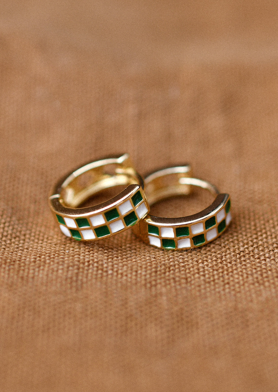 A pair of gold hoop earrings with green and white enamel checker pattern.