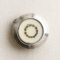 White Wreath: A round silver-tone measuring tape with cream enamel and wreath design.