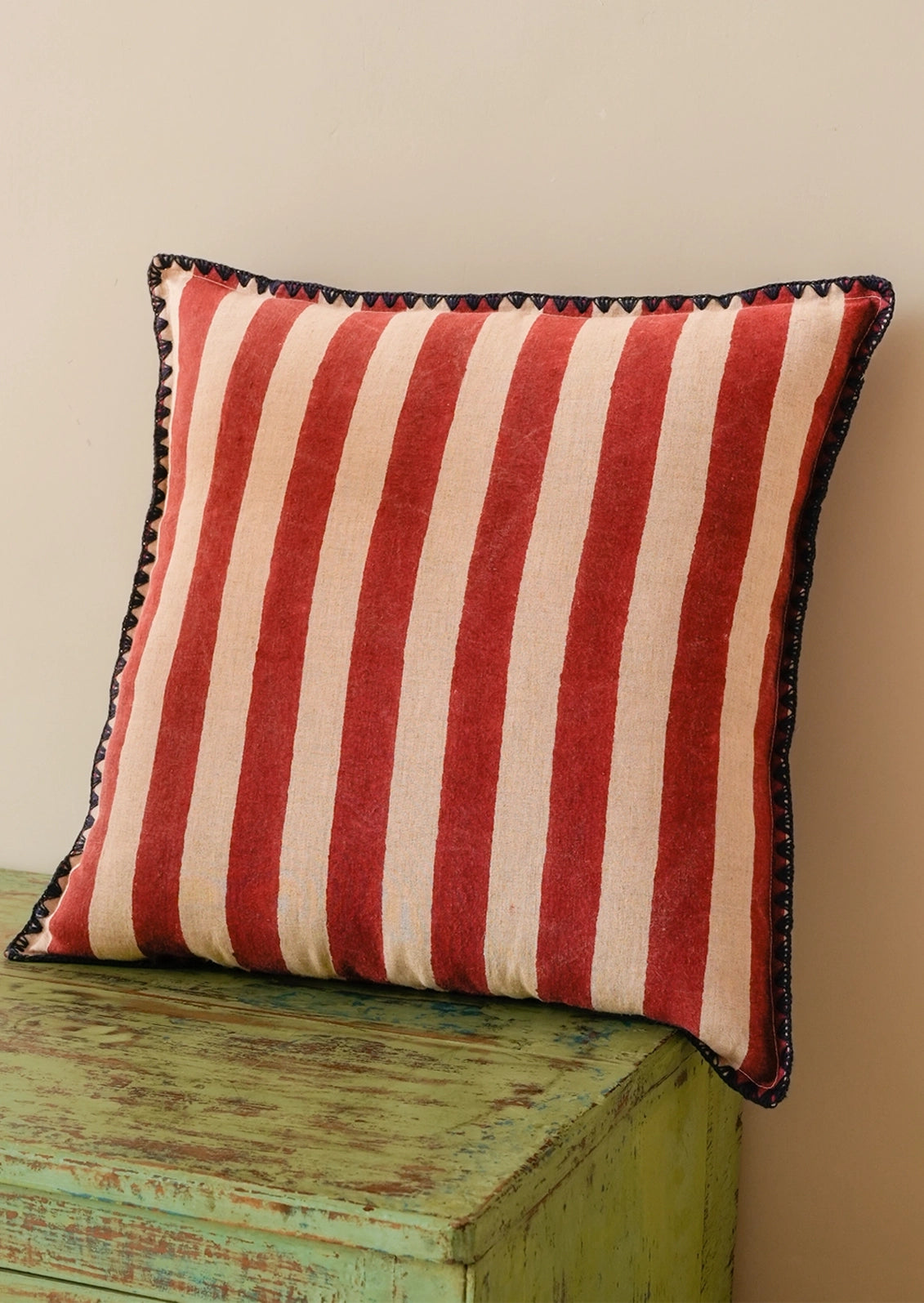 A square throw pillow with vertical red and cream stripes and a navy embroidered border.