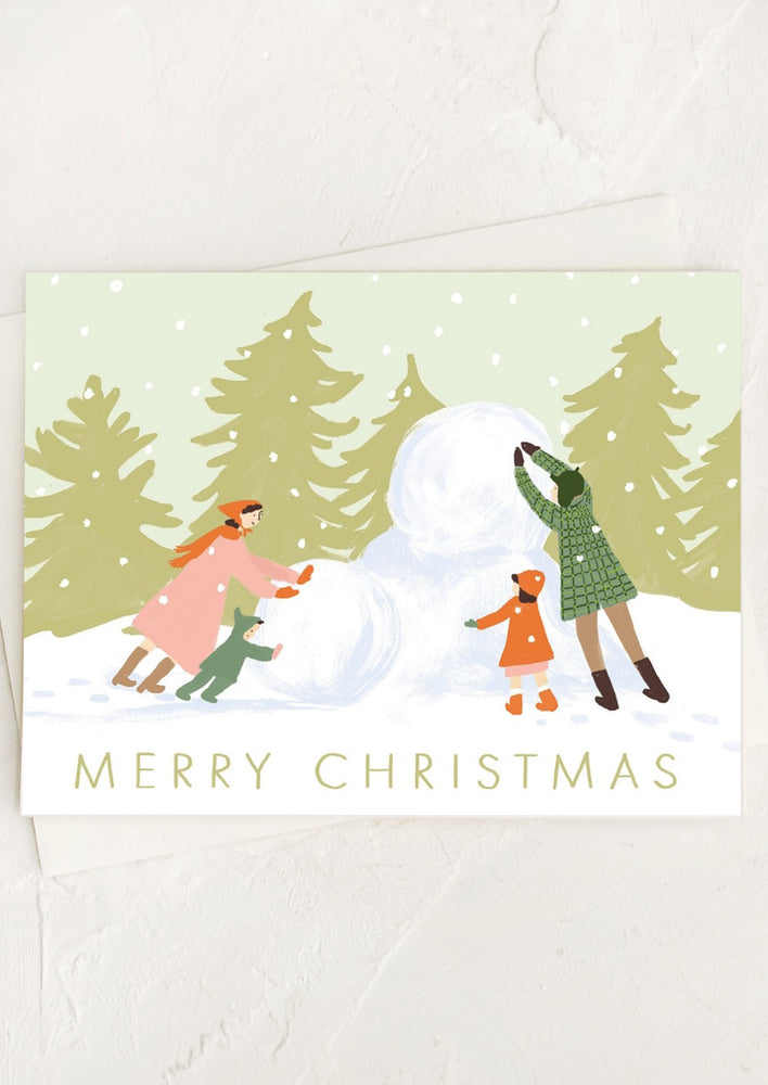 A greeting card with illustration of a man, woman and child building a snowman.