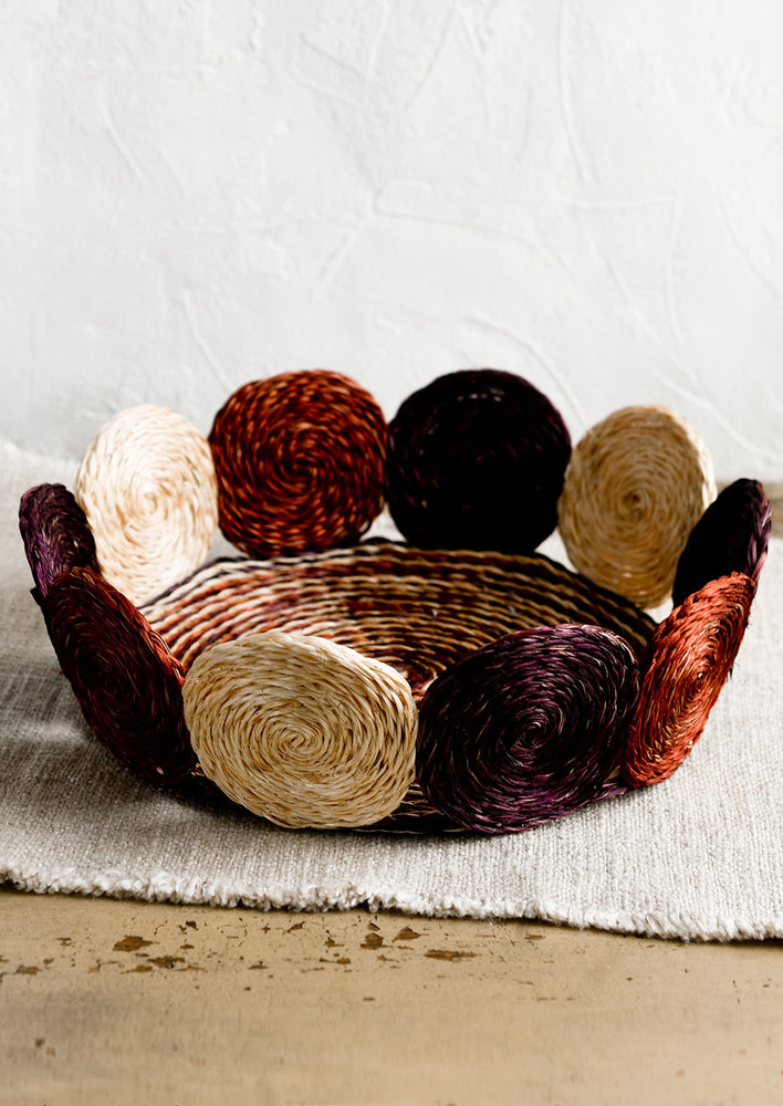 A round, shallow basket with woven circular border design in fig multi.
