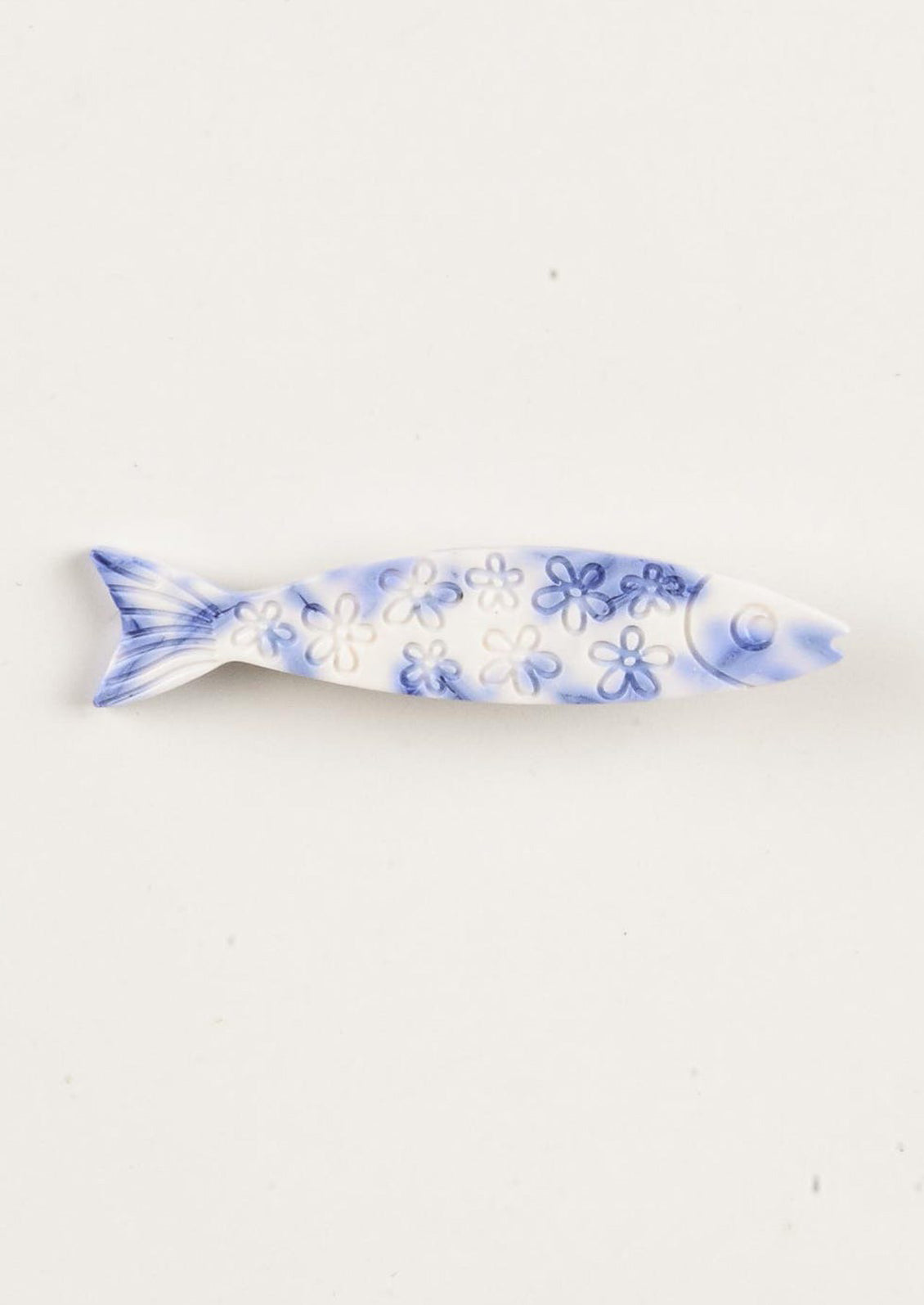 A blue and white barrette in the shape of a sardine with floral carved pattern.