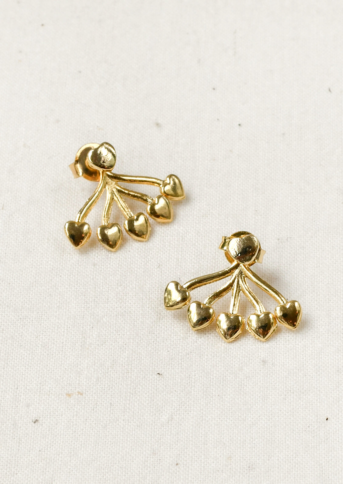 A pair of gold earrings with a heart shaped stud and five small hearts hanging below that attach on the back of the ear. 
