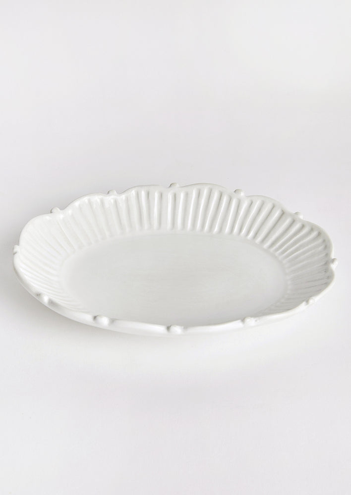An oval shaped tray with ruffled and pleated border with ball detail around edges.